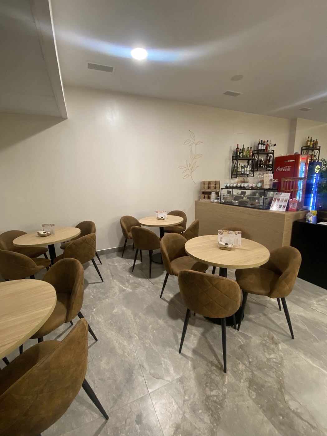 Sala interior de NamasTé Café con mesas redondas, sillas en tono mostaza y suelo de mármol